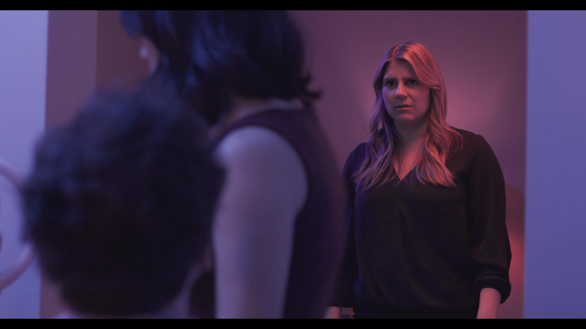 The protagonist of Method and Madness standing in a doorframe with colored lighting. She looks horrified at the antagonist and his associate.