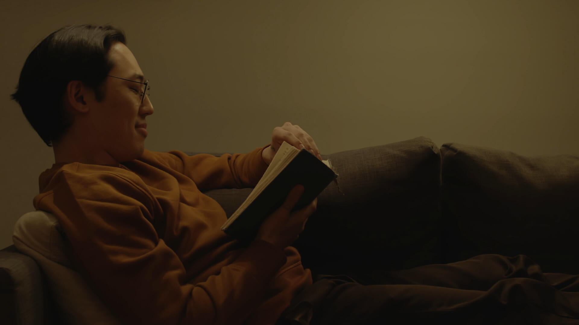 One-Sided Window Still 1 The leading man lounges on a couch, reading a book.