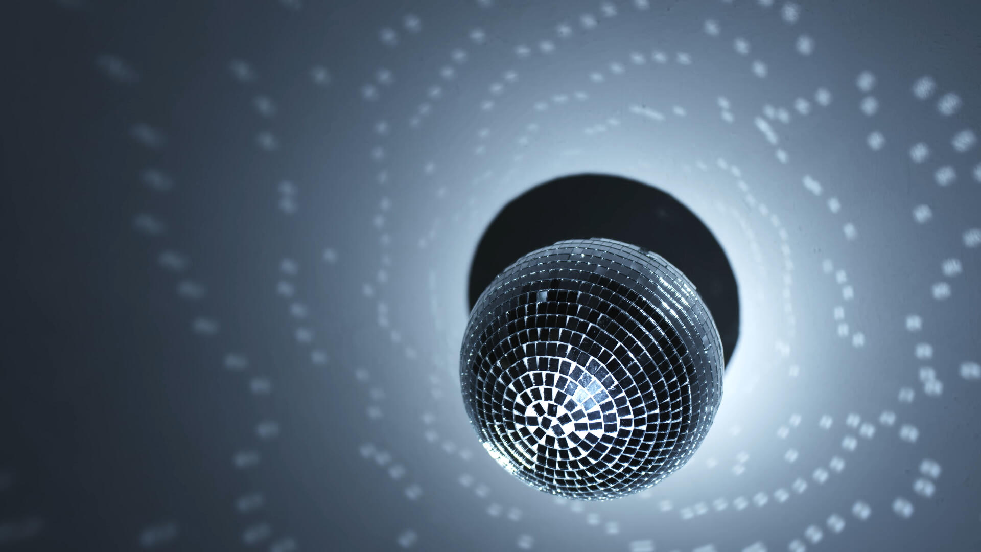 A disco ball is lit up by a pointed light offscreen. Reflections from the mirrors dance around on the ceiling.