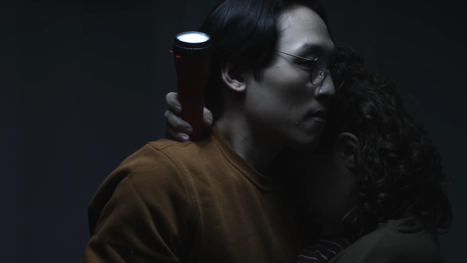One-Sided Window Still 2 The leading couple embraces, lit only by the light of a flashlight pointed up at the ceiling.